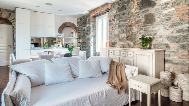 A modern bedroom with a stone wall, a white sofa, and a small bedside table. - Stunning Central Como apt by JOIVY  (Como)
