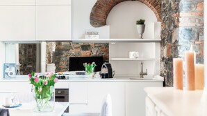 A modern kitchen with white cabinetry, a brick arch above the stove, and a stone wall in the background. - Stunning Central Como apt by JOIVY  (Como)