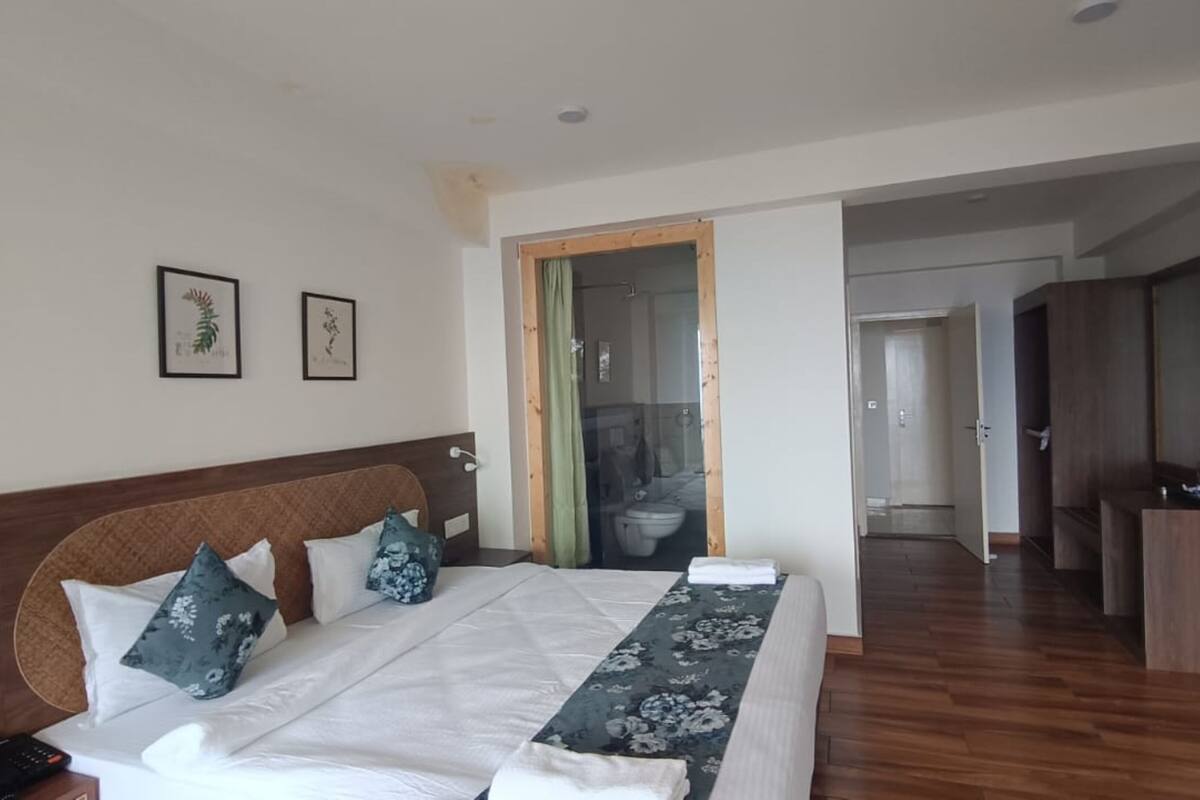 Een hotelkamer met een groot bed, een houten hoofdeinde, een badkamer zichtbaar door een glazen deur en een houten vloer.