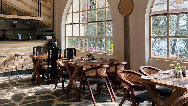 Un comedor amplio con techos altos, ventanas grandes y una mesa de madera central rodeada de sillas.