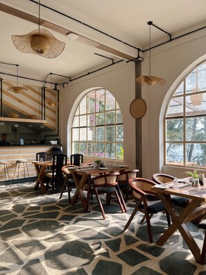 Un comedor amplio con techos altos, ventanas grandes y una mesa de madera central rodeada de sillas.