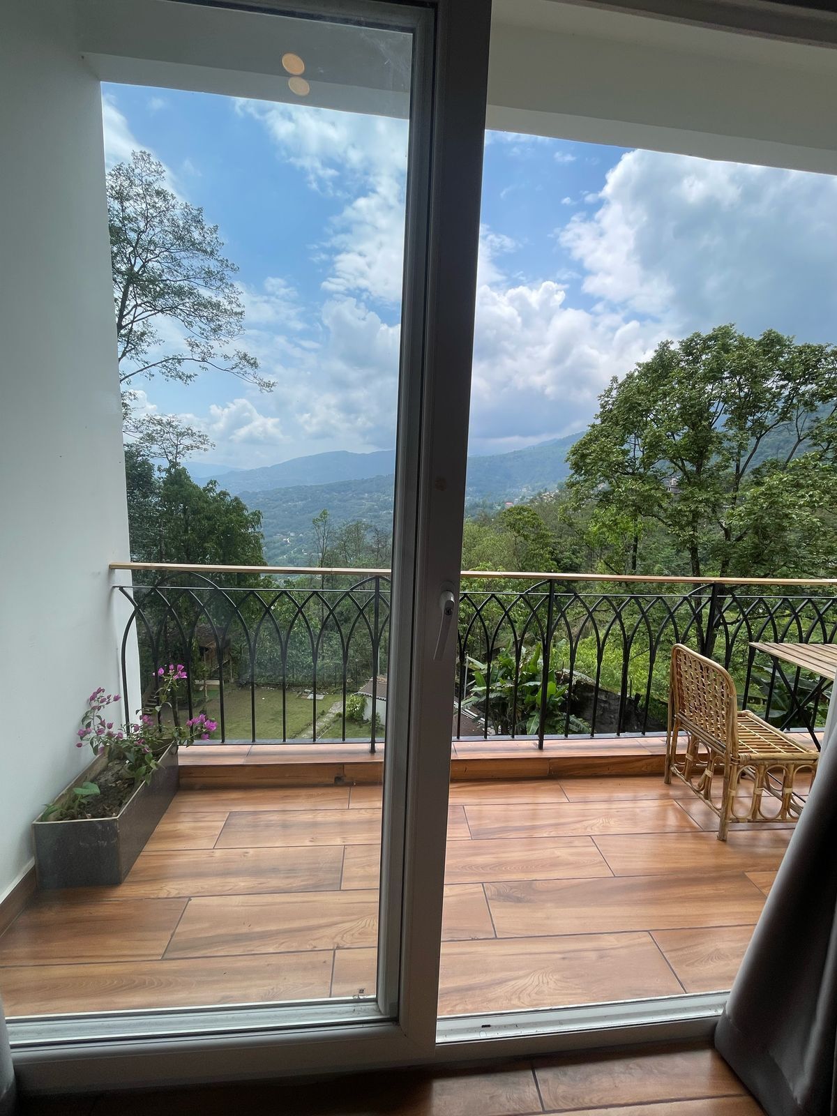 Un balcon offrant une vue sur un paysage montagneux, avec un plancher en bois et une chaise en osier.
