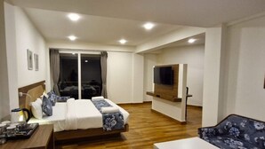 Una habitación de hotel con una cama, un televisor, un sofá y una mesa de comedor.