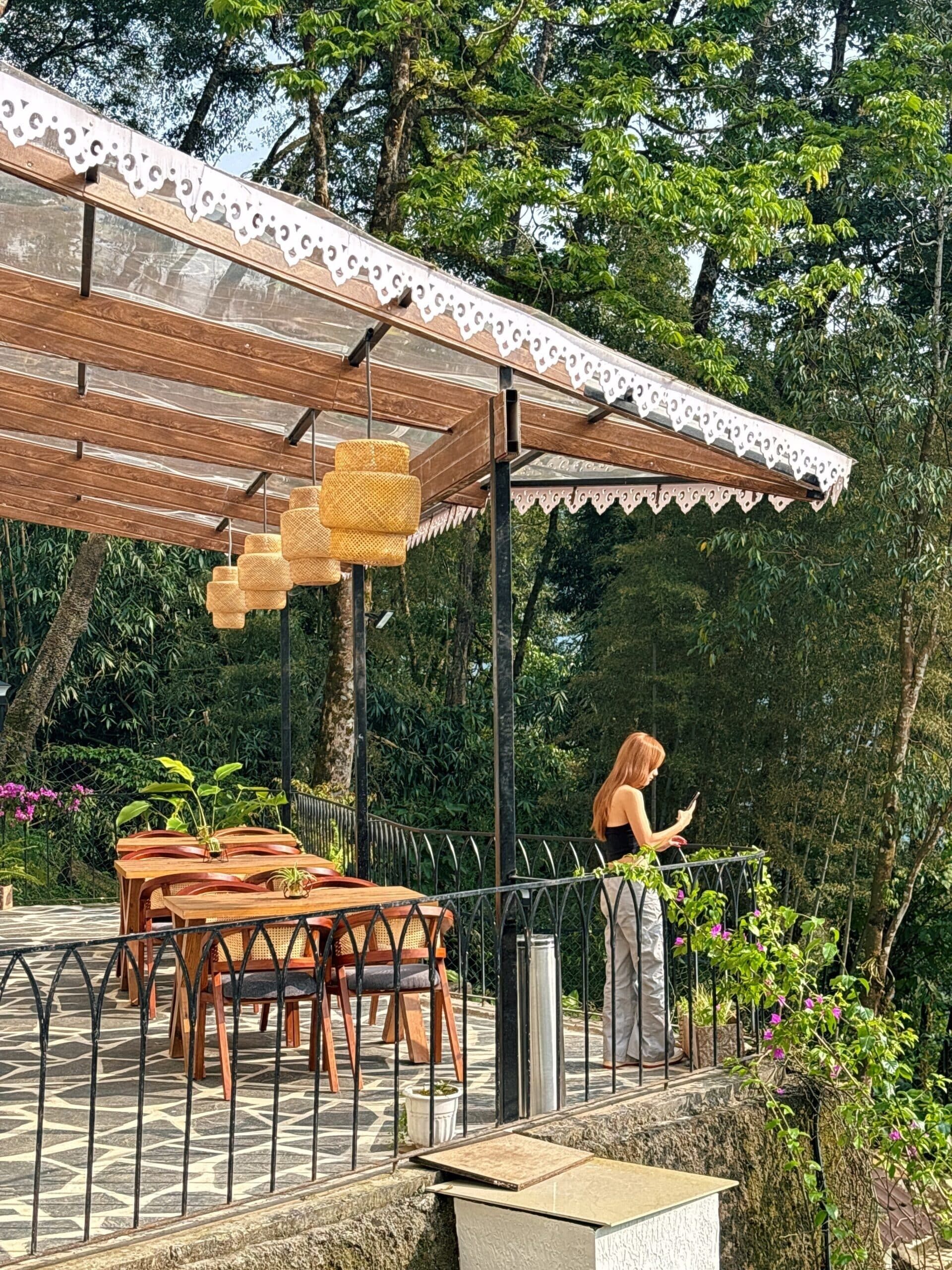 An outdoor patio with wooden tables and chairs, a covered area with a patterned roof, and hanging wicker lamps.