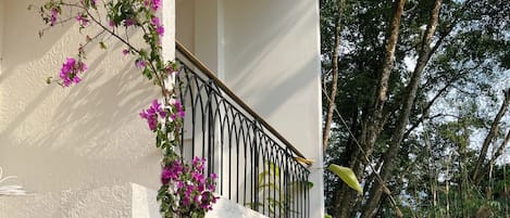 Un edificio de dos pisos con balcón, mobiliario exterior y un jardín lleno de flores rosas.