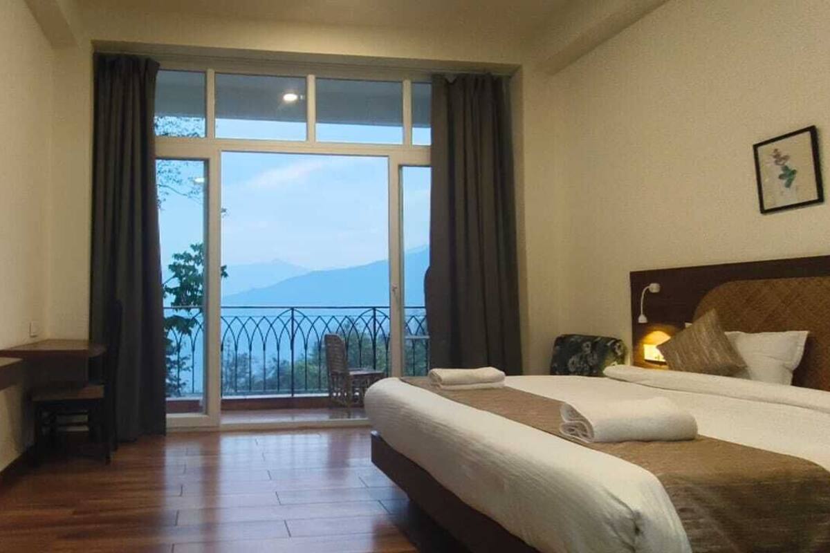 Een hotelkamer met een groot raam, een aan de muur bevestigde televisie, een bed en een klein tafeltje.