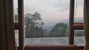 Una habitación con un ventanal grande, un banco de madera y vistas a árboles y montañas.