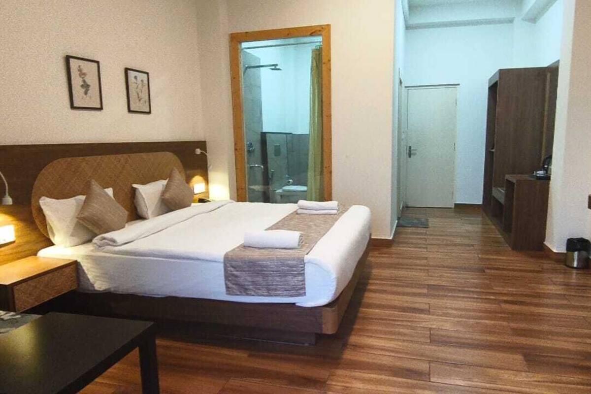 Een hotelkamer met een bed, nachtkastje, lamp, televisie en houten vloer.