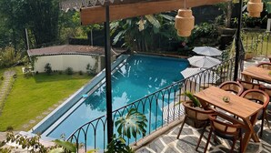 Un área junto a la piscina con vistas a montañas, una pérgola con luces colgantes y mobiliario exterior.