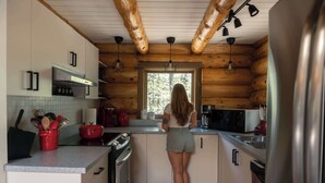 A woman in a kitchen with wooden walls, a window, and modern appliances.