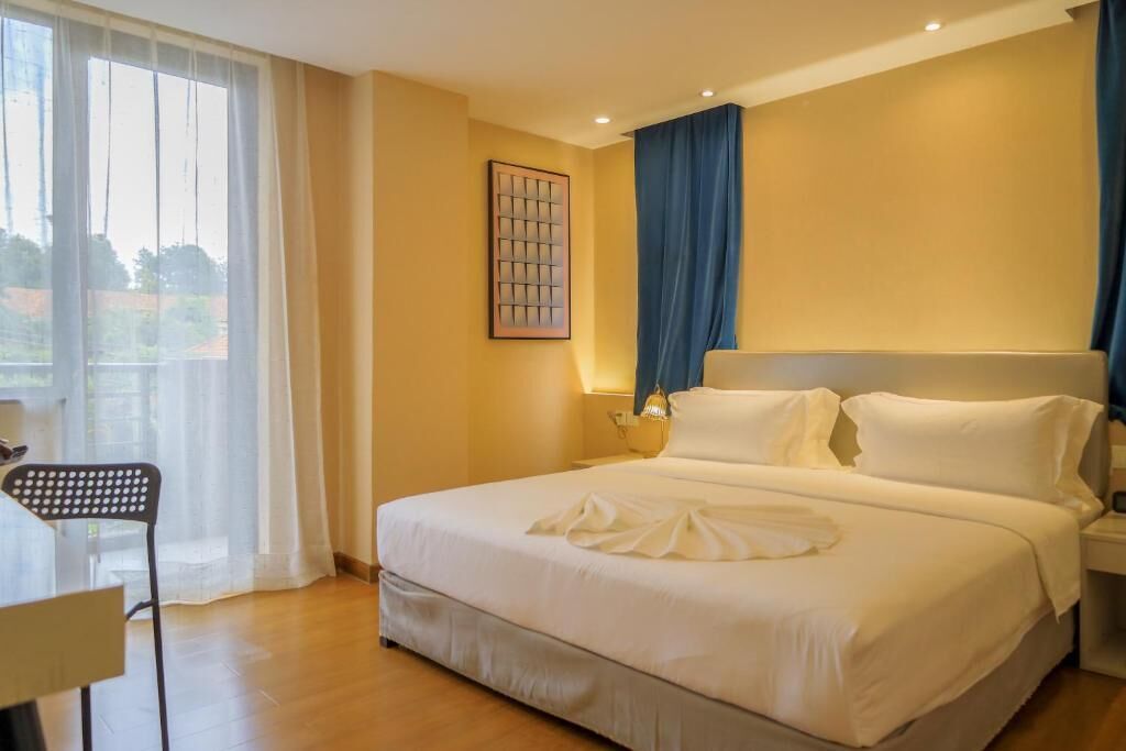 Una habitación de hotel con una cama grande, una silla, un escritorio y una ventana con cortinas.