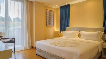 Una habitación de hotel con una cama grande, una silla, un escritorio y una ventana con cortinas.