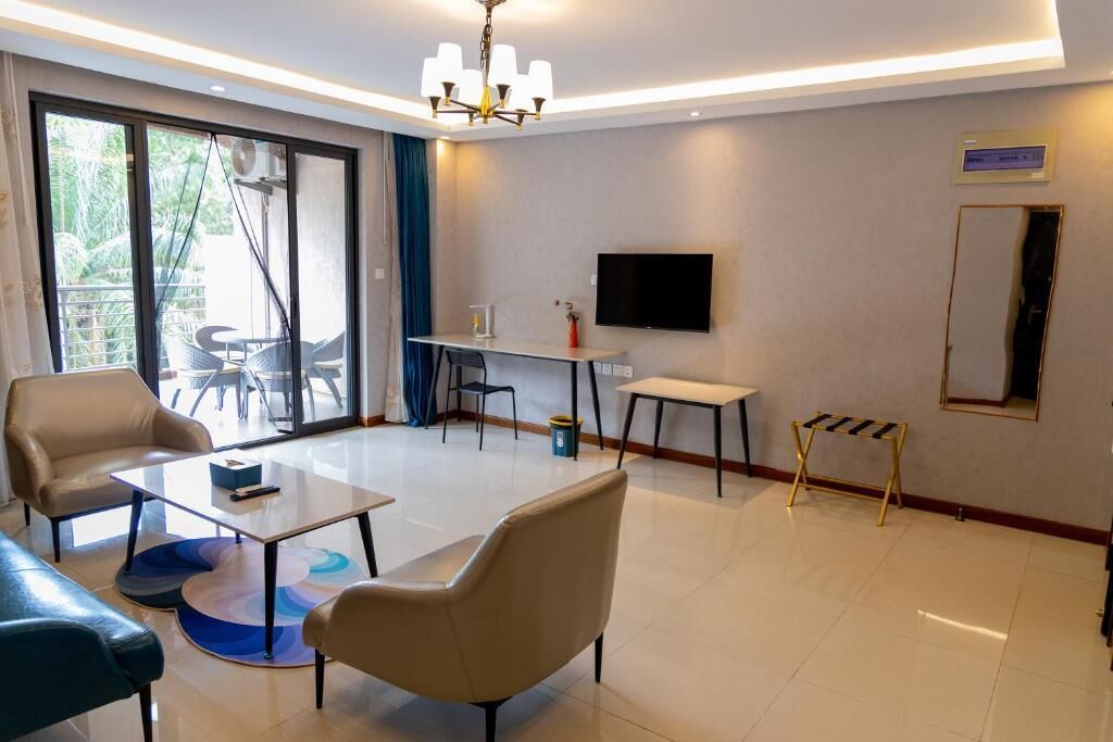 A modern hotel room with a sofa, armchair, coffee table, TV, and a balcony with outdoor furniture.