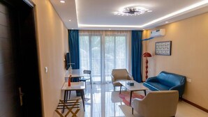 A modern living room with a sofa, chairs, a coffee table, and a dining area with a table and chairs. - Harmony Hotel Kampala (Kampala)
