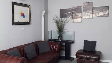 Ein modernes Wohnzimmer mit Ledersofa, Pouf, Glastisch und einem Blumentopf.