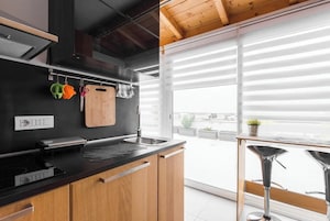 Una cocina moderna con encimera negra, armarios de madera y un amplio ventanal con vistas a un jardín en la azotea.