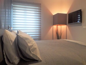 A bedroom with a bed, pillows, a bedside lamp, and a window with blinds. - Attico con vista Ciampino Roma  (Ciampino)