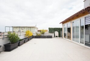 A rooftop terrace with potted plants, a white chair, and a glass door leading to a covered area. - Attico con vista Ciampino Roma  (Ciampino)