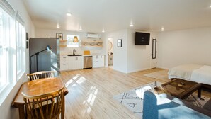 A modern apartment with a kitchen, dining area, and living room. It features a large window, a flat-screen TV, and a sofa. - Adorable Studio - Private Patio - Dream Kitchen (Waco)
