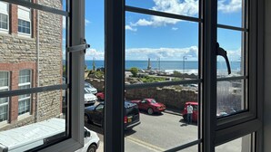 A view through a window with a stone building, parked cars, and a clear sky. - The Yacht Inn (Penzance)