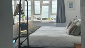A bedroom with a bed, a window with a view of the sea, a ceiling fan, and a radiator. - The Yacht Inn (Penzance)
