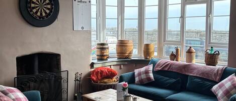 Un salon chaleureux avec des canapés turquoise, un jeu de fléchettes, une cheminée et de grandes fenêtres donnant sur la ville.