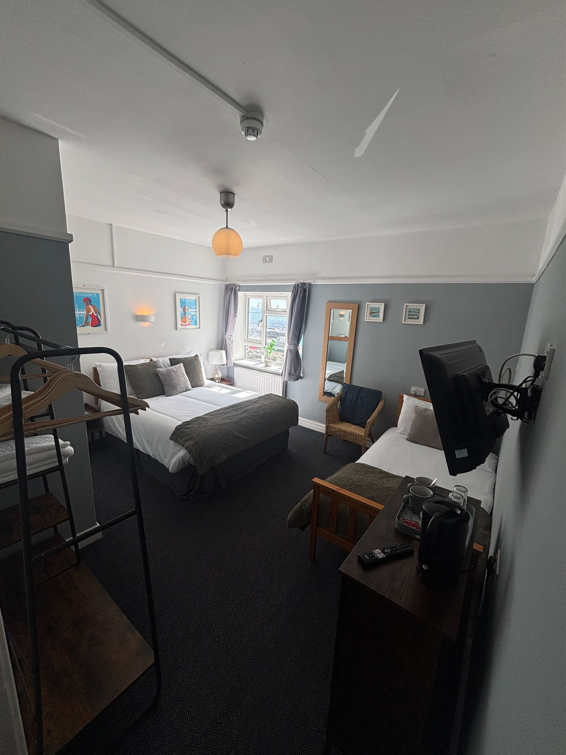 Habitación de hotel con cama, sofá, televisión, escritorio y una bandeja con objetos, además de una ventana con cortinas.