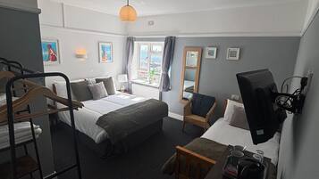 Habitación de hotel con cama, sofá, televisión, escritorio y una bandeja con objetos, además de una ventana con cortinas.