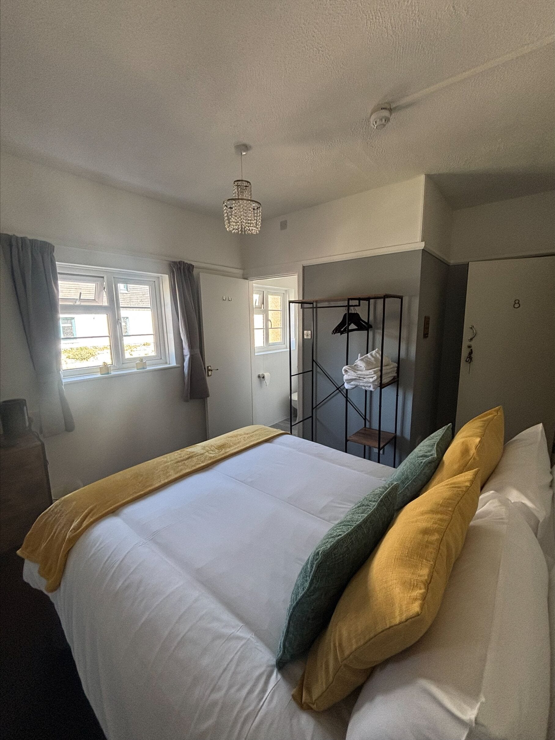 A hotel room with a bed, a wardrobe, a hanging rack, and a window with curtains.