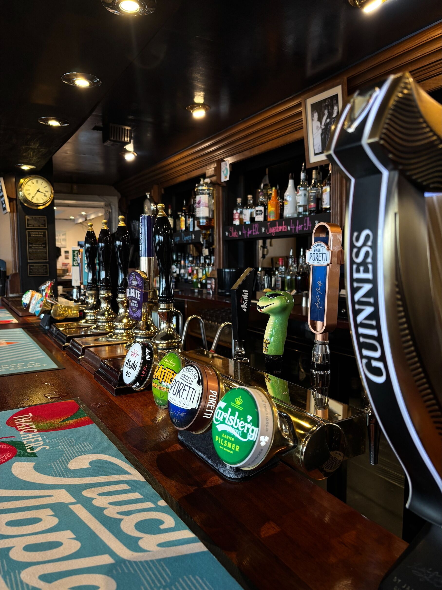 A bar with multiple beer taps, a clock, and shelves stocked with bottles.