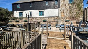 A building with a stone facade and a wooden deck with picnic tables. - The Yacht Inn (Penzance)