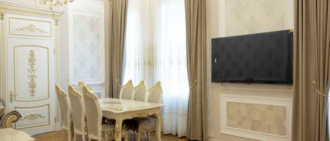 A dining room with a white table and chairs, a chandelier, and a flat-screen TV mounted on the wall.