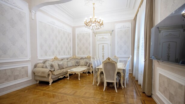 A room with a herringbone floor, a white sofa, a dining table with chairs, and a chandelier.