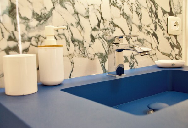 A bathroom with a blue sink, a marble wall, and a white soap dispenser. - Theater Luxury Apartment (Marsala)