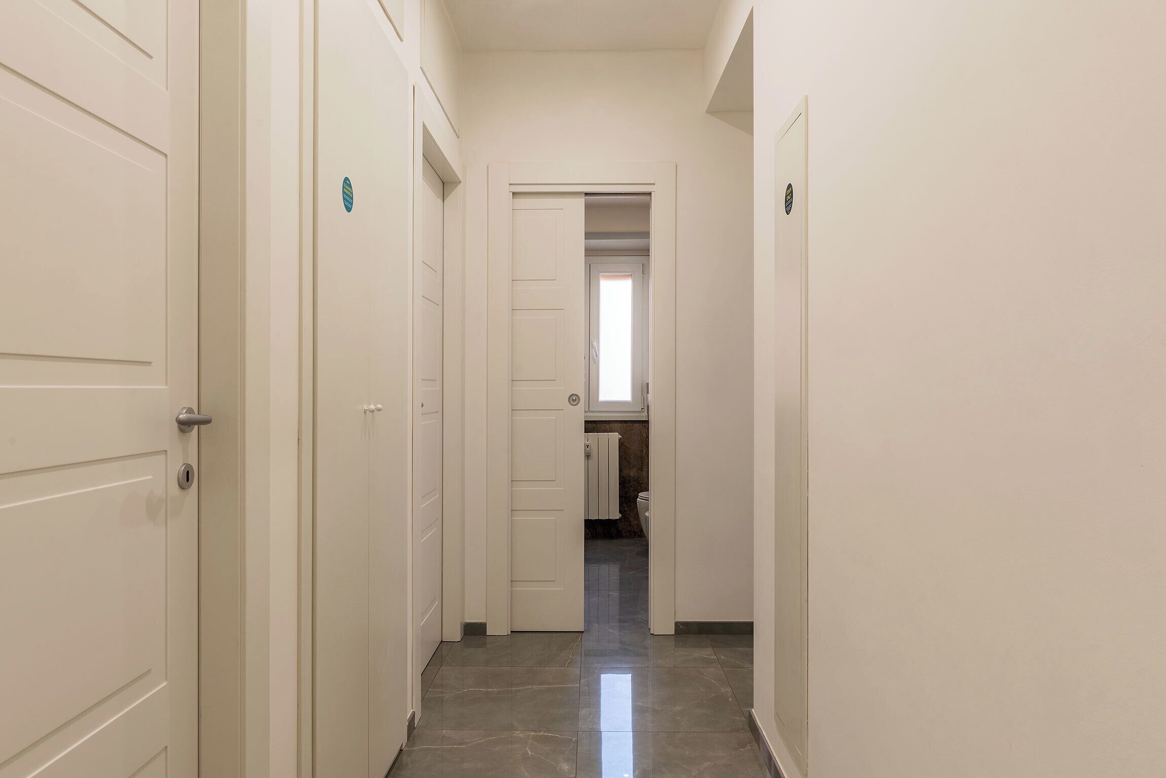 Un pasillo estrecho con puertas blancas que conduce a un baño con inodoro y lavamanos.