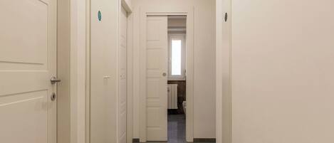 Un pasillo estrecho con puertas blancas que conduce a un baño con inodoro y lavamanos.