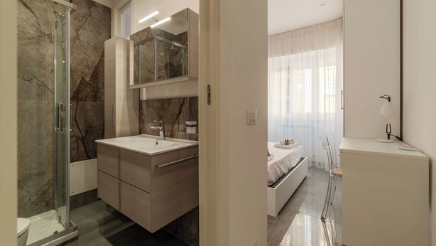 Une salle de bain moderne avec une douche en verre, des murs en marbre et un meuble-lavabo blanc.