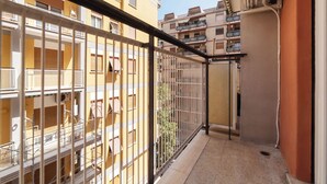 Un balcon étroit avec des balustrades en métal, un sol carrelé et une vue sur les immeubles voisins, qui sont également dotés de balcons.