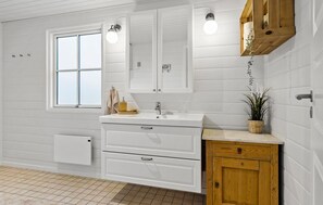 Bathroom features a large window, white vanity with sink and storage, and a wooden cabinet with a plant.