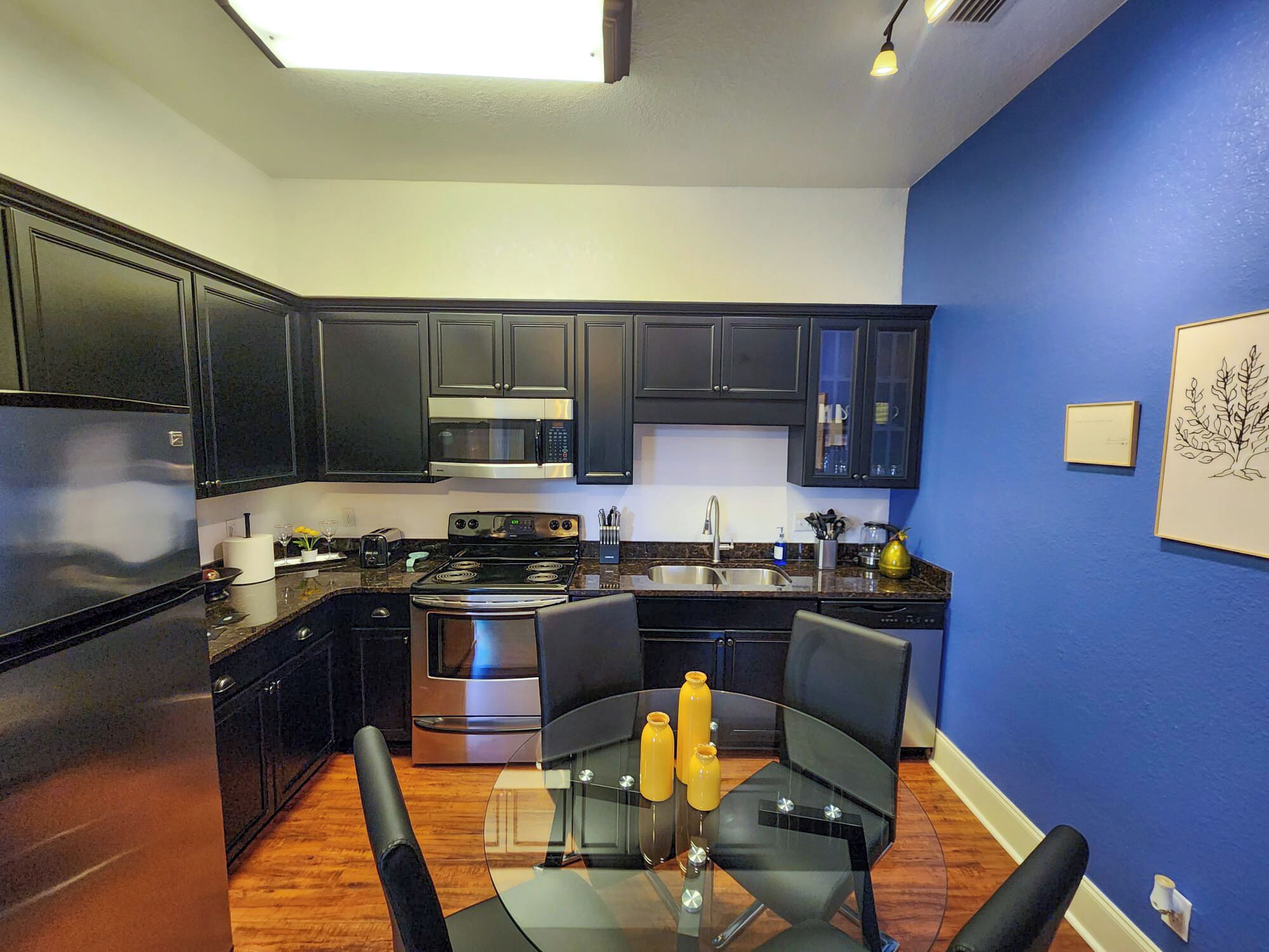 Una cocina moderna con gabinetes oscuros, electrodomésticos de acero inoxidable y una pared de acento azul.