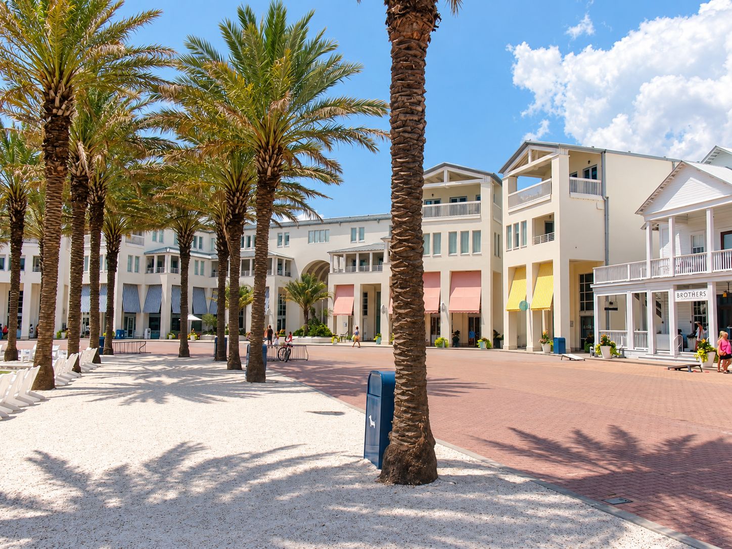 A hotel courtyard with palm trees, a covered walkway, and a building with a sign 'BROTHERS'.