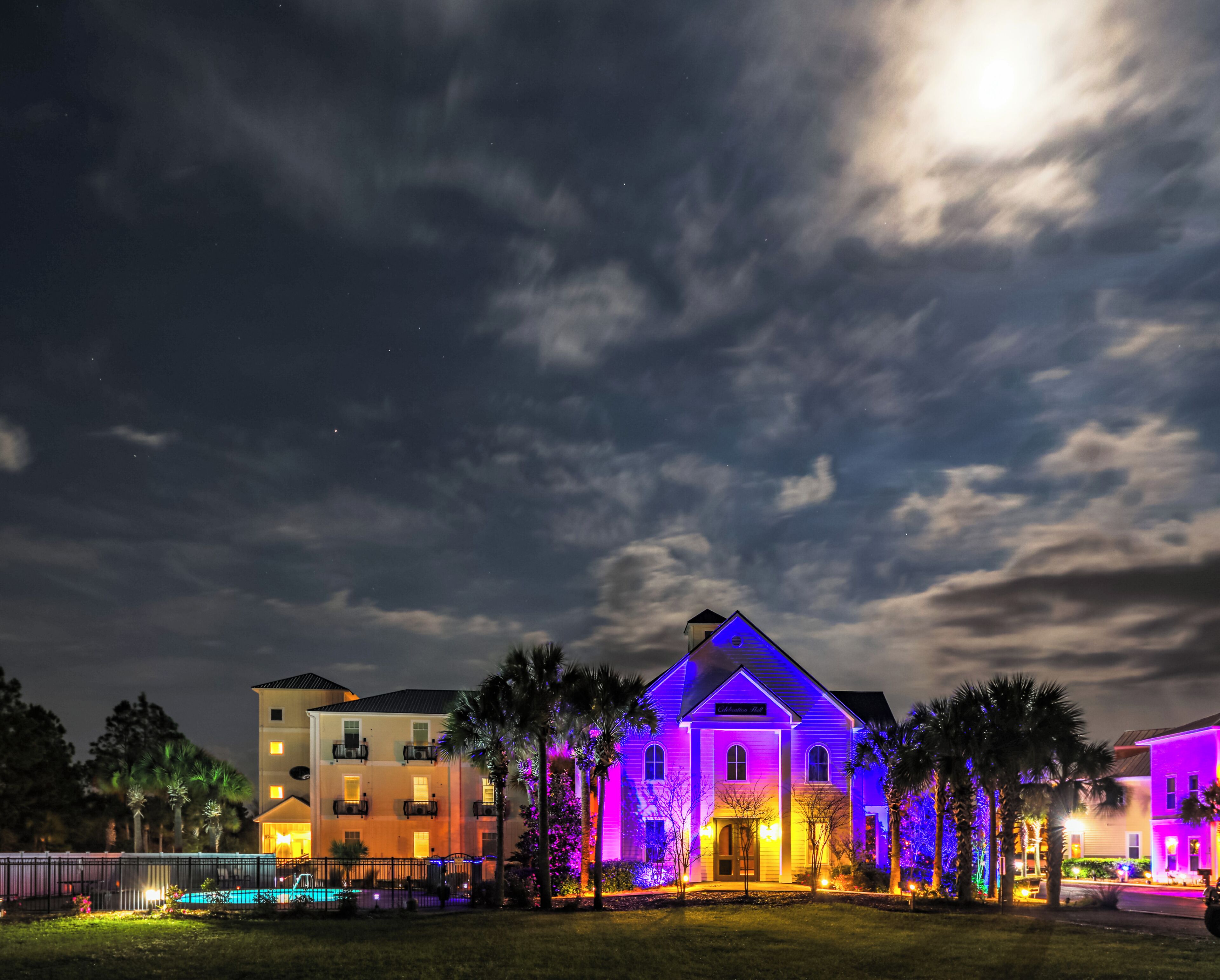 A hotel with a well-lit entrance, a swimming pool, and a large building with colorful lighting.