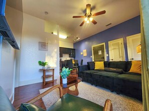 A modern living room with a dark green sofa, a glass coffee table, and a ceiling fan.