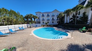 A swimming pool with a brick deck, surrounded by lounge chairs and a fence.