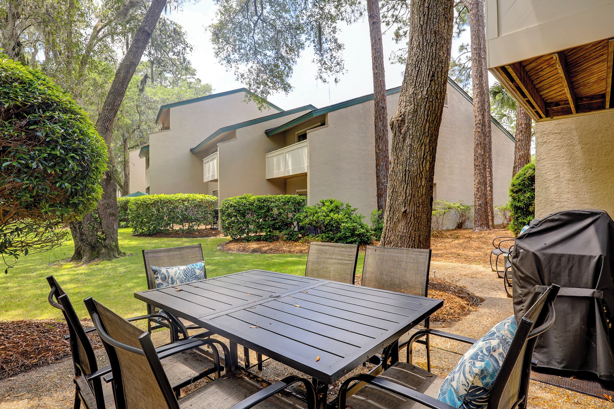 A patio with a table and chairs, surrounded by trees and a building with balconies.