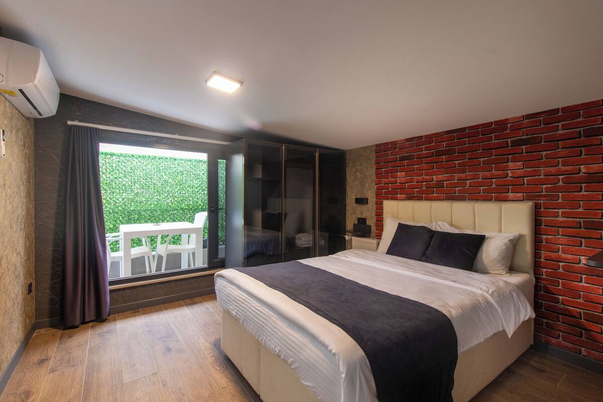 A modern bedroom with a large bed, a glass door leading to a balcony, and a brick wall.