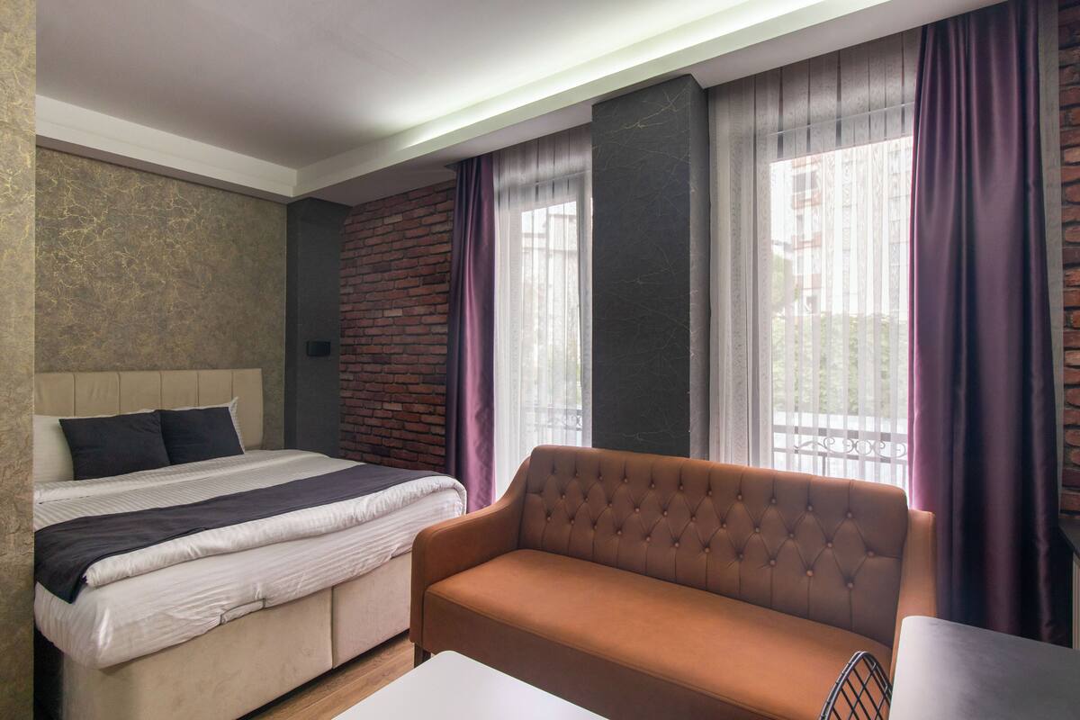 A modern hotel room with a bed, sofa, and a small table.