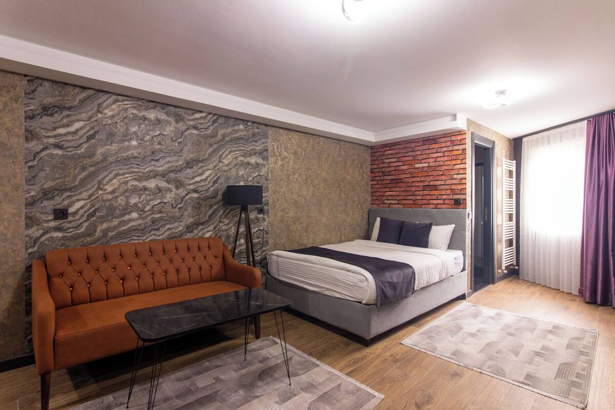 A modern bedroom with a marble-patterned wall, a brick accent wall, a sofa, a bed, and a small table.