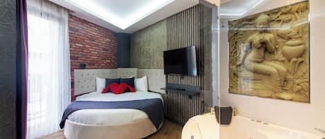 Un dormitorio moderno con cama curvada, un ventanal con cortinas, televisor de pantalla plana, televisor instalado en la pared, bañera y un elemento decorativo en la pared.