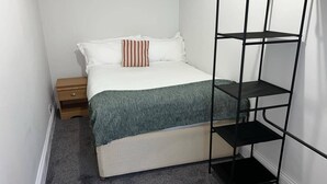 Een compacte, verzorgde slaapkamer met een bed, nachtkastje, opbergmeubel en een vloerkleed.
